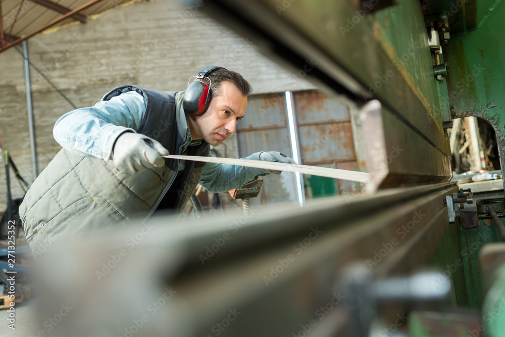 worker passing sheet metal through industrial machine