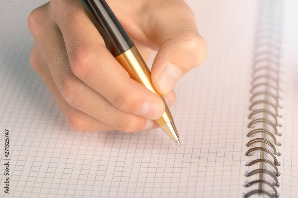 Teen writes black yellow pen in a checkered notebook Teen writes black yellow pen in a checkered notebook