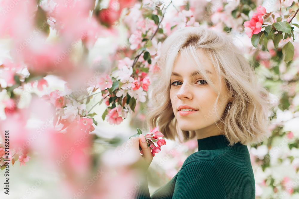 Close up portrait of young pretty caucasian curly blondie model posing outdoors in pink blossom garden. Beauty, nature concept Close up portrait of young pretty caucasian curly blondie model posing outdoors in pink blossom garden. Beauty, nature concept