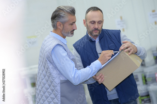 manager showing clipboard to worker in warehouse