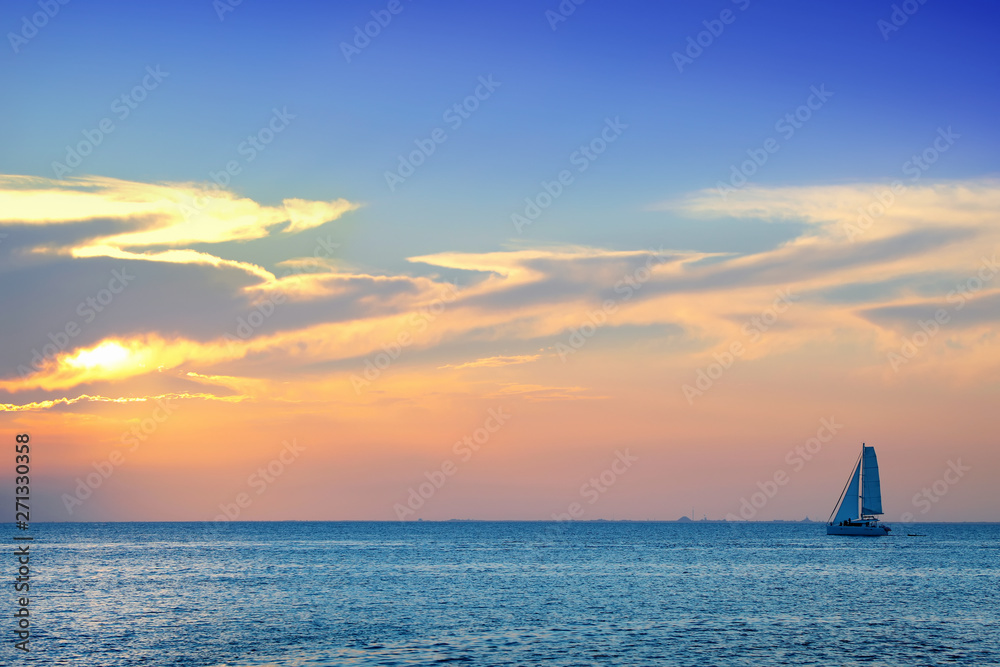 Colorful seascape image with shiny sea and sailboat over cloudy sky and sun during sunset in Cozumel, Mexico