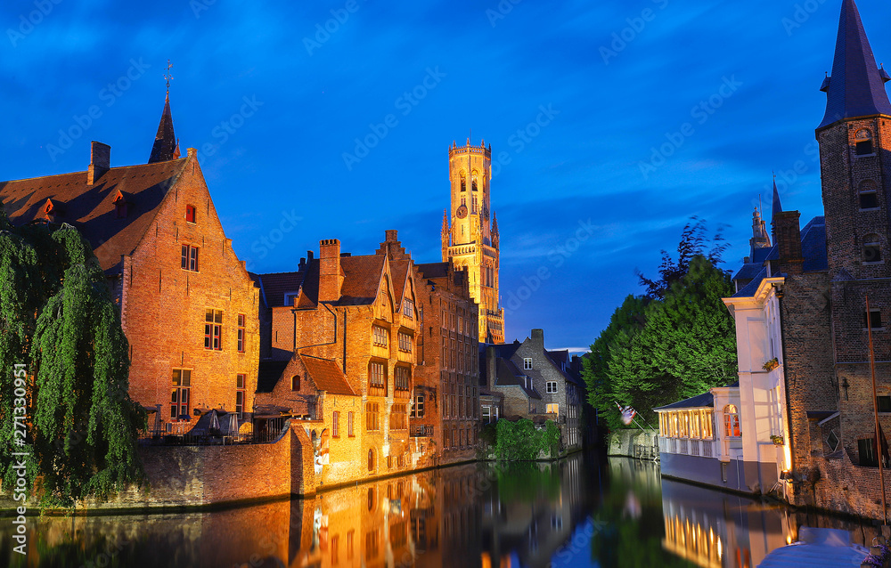 Famous view of Bruges tourist landmark attraction - Rozenhoedkaai canal with Belfry and old houses along canal with tree in the night. Belgium