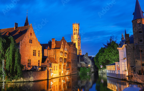 Famous view of Bruges tourist landmark attraction - Rozenhoedkaai canal with Belfry and old houses along canal with tree in the night. Belgium