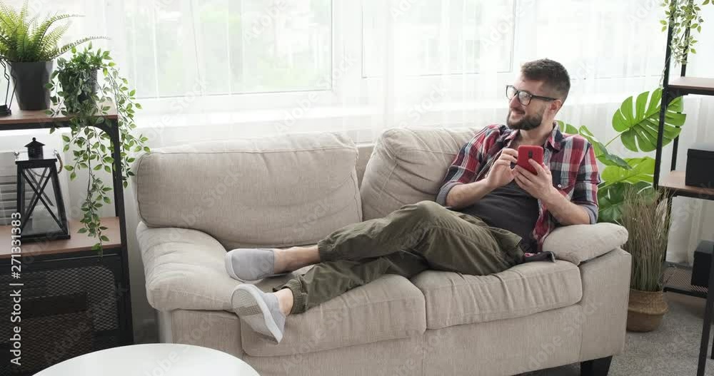 Smiling young man using mobile phone on sofa at home Smiling young man using mobile phone on sofa at home