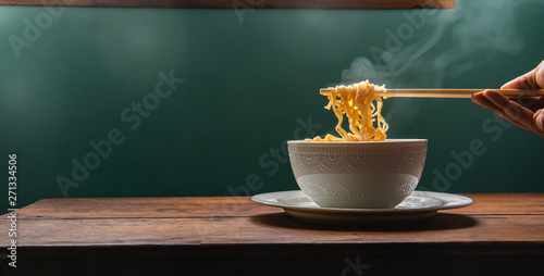 Noodle on chopsticks with light and smoke on the wooden board.