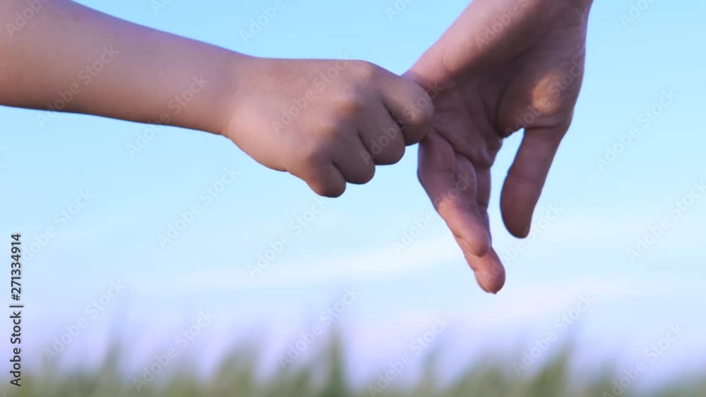 The child holds the parent's finger. Hand of mother and baby on a background of blue sky.