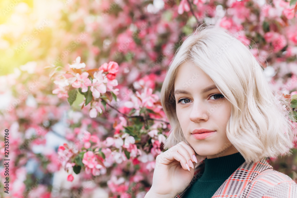 Close up portrait of young pretty caucasian curly blondie model posing outdoors in pink blossom garden. Beauty, nature concept