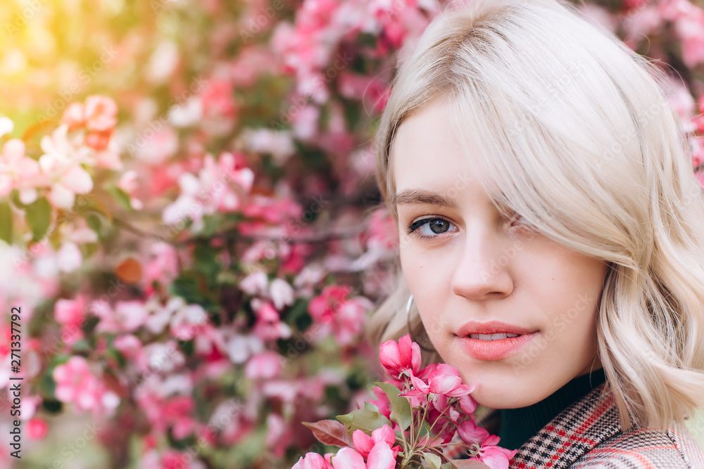 Close up portrait of young pretty caucasian curly blondie model posing outdoors in pink blossom garden. Beauty, nature concept Close up portrait of young pretty caucasian curly blondie model posing outdoors in pink blossom garden. Beauty, nature concept