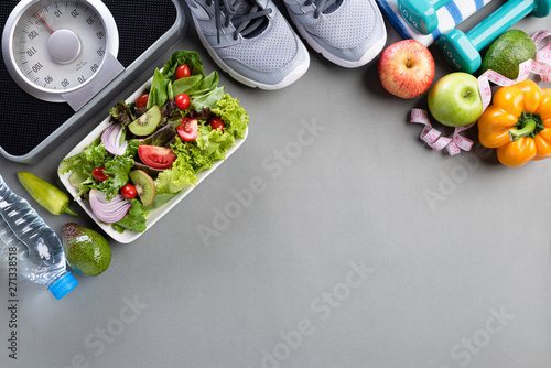 Healthy lifestyle, food and sport concept. Top view of athlete's equipment Weight Scale measuring tape green dumbbell, sport water bottles, fruit and vegetables on gray background.