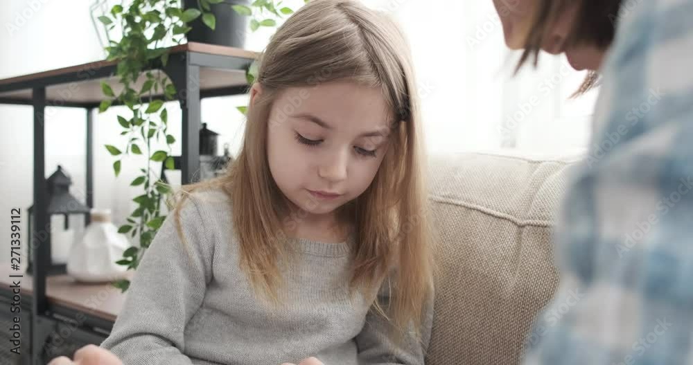 Mother with little daughter using calculator on sofa at home Mother with little daughter using calculator on sofa at home