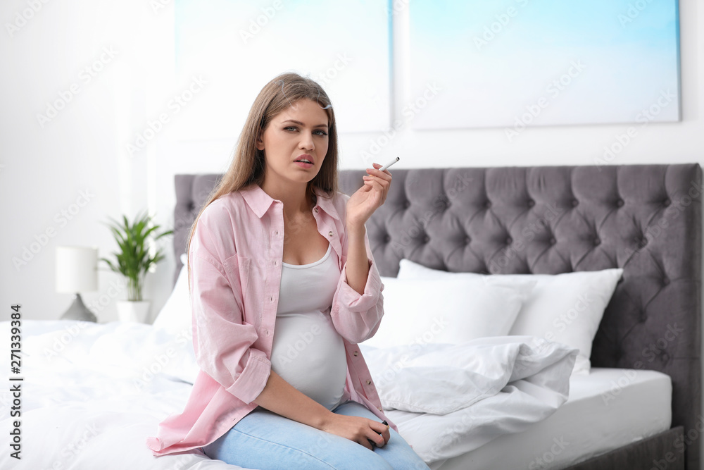 Young pregnant woman smoking cigarette in bedroom. Harm to unborn baby Young pregnant woman smoking cigarette in bedroom. Harm to unborn baby