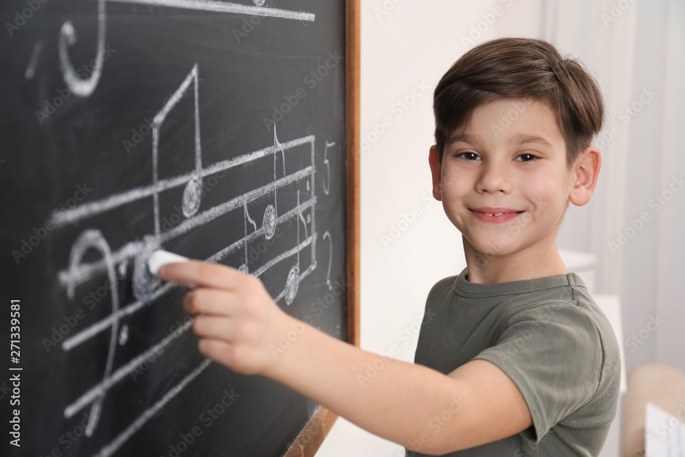 Little boy writing music notes on blackboard in classroom Little boy writing music notes on blackboard in classroom