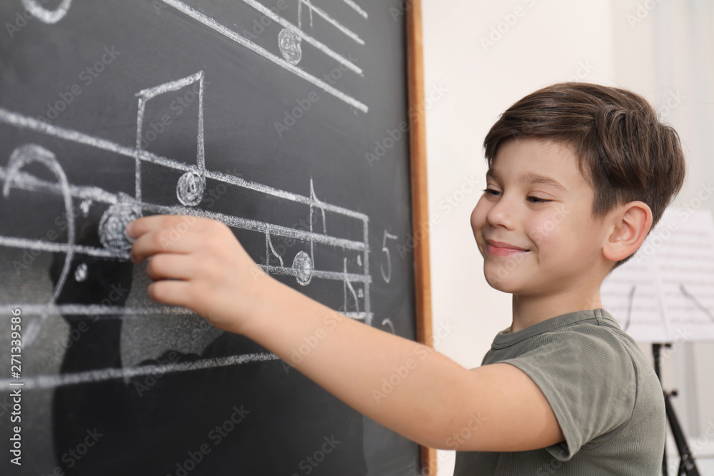 Little boy writing music notes on blackboard in classroom Little boy writing music notes on blackboard in classroom