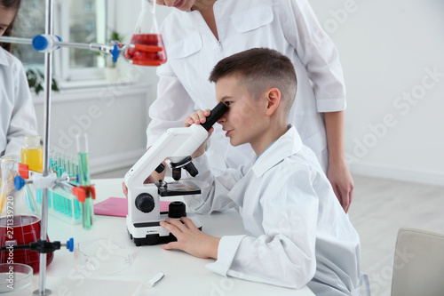 Schoolboy looking through microscope at table in chemistry class