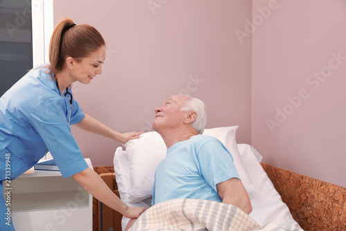 Nurse assisting senior man on bed in hospital ward