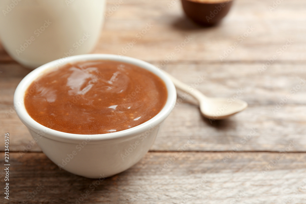 Bowl with caramel sauce on wooden table, closeup. Space for text Bowl with caramel sauce on wooden table, closeup. Space for text