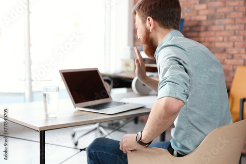 Young man using video chat on laptop in home office. Space for text