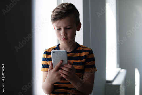 Sad little child with smartphone indoors. Danger of internet