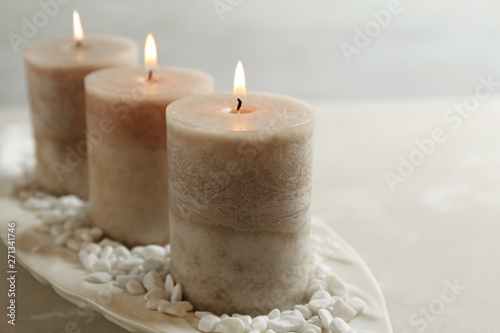 White plate with three burning candles and rocks on table, space for text