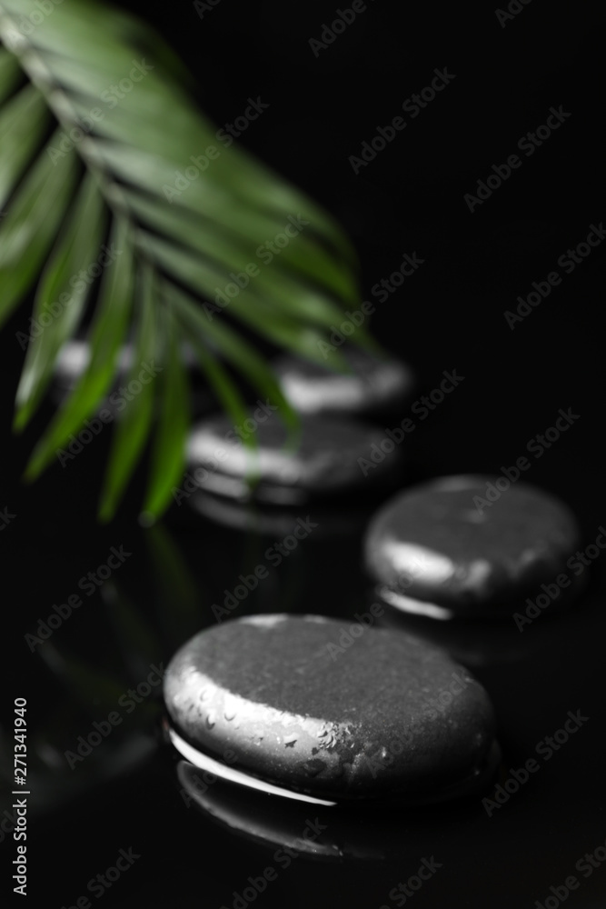 Composition with wet spa stones and green leaf on black background. Space for text Composition with wet spa stones and green leaf on black background. Space for text