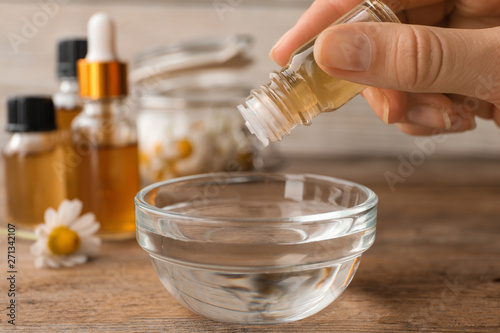 Woman dripping essential oil into bowl on table, closeup