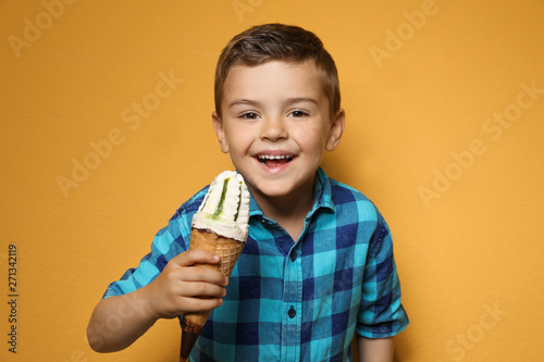 Adorable little boy with delicious ice cream against color background