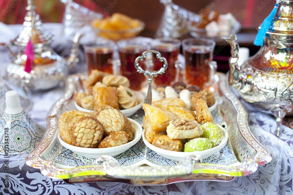 Oriental tea tray and cookies symbolising Moroccan hospitality, Islamic holidays food with decoration. Ramadan kareem. Eid mubarak. Oriental hospitality concept. Tea glasses and pot, traditional delig