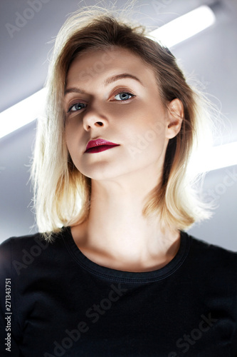 Portrait of a young beautiful woman with blond hair and red lips. Back light, low angle light, long lamp.