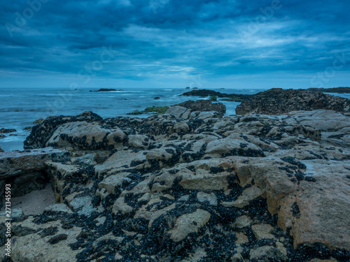 Dusk on the rocky beach with dramatic clouds and dark moody sky. Long exposure.