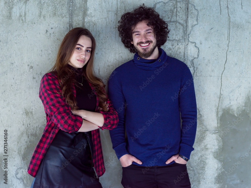 portrait of casual business couple in front of a concrete wall