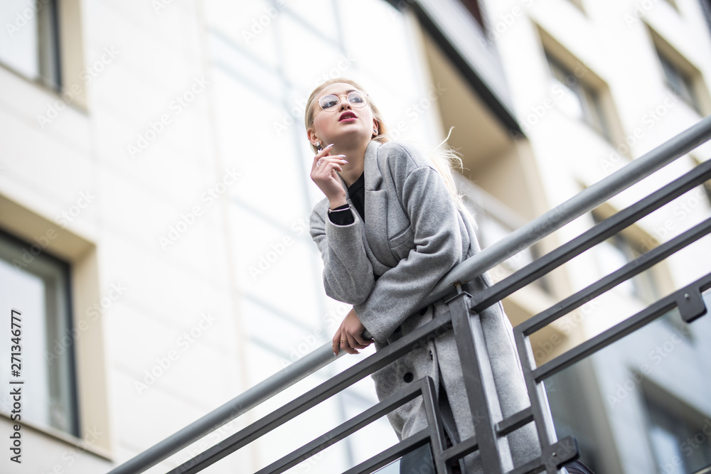 Happy fashion woman in gray coat leaning on handrail in city street. Happy fashion woman in gray coat leaning on handrail in city street.