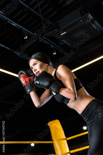 low angle view of confident young woman boxing while standing in boxing gloves in gym