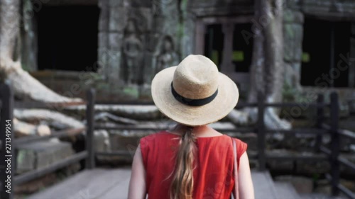 Following caucasian woman exloring Ta Prohm temple and taking photo of iits exterior including giant banyan roots growing on its gallery. Cambodia photo