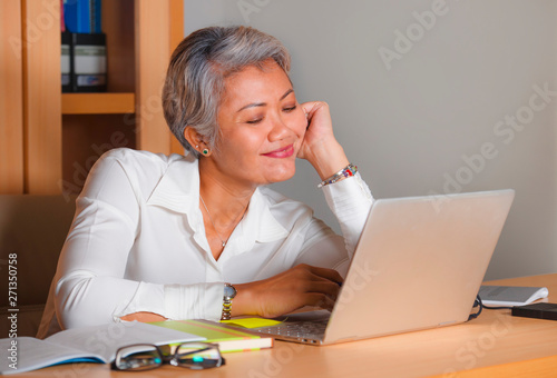 corporate job lifestyle portrait of happy and successful attractive middle aged Asian woman working at office laptop computer desk satisfied and efficient in business success
