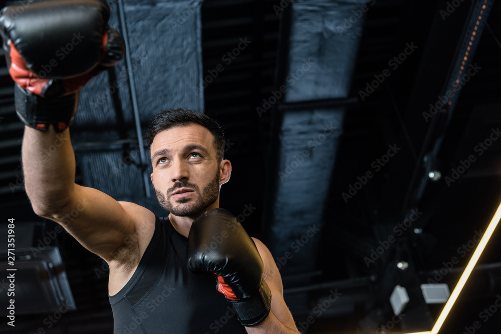 low angle view of handsome man exercising in boxing gloves