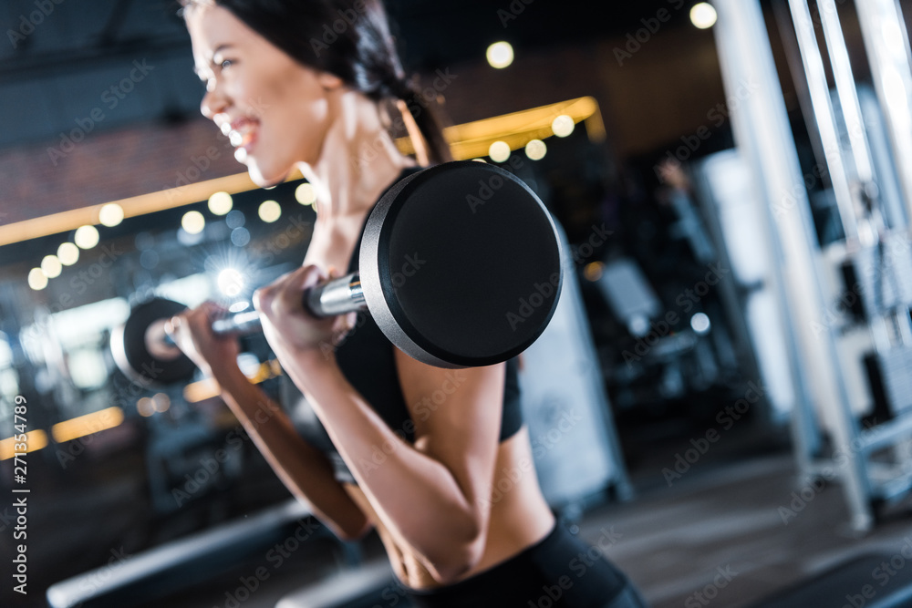 Selective focus of young woman working out with heavy barbell in gym Selective focus of young woman working out with heavy barbell in gym