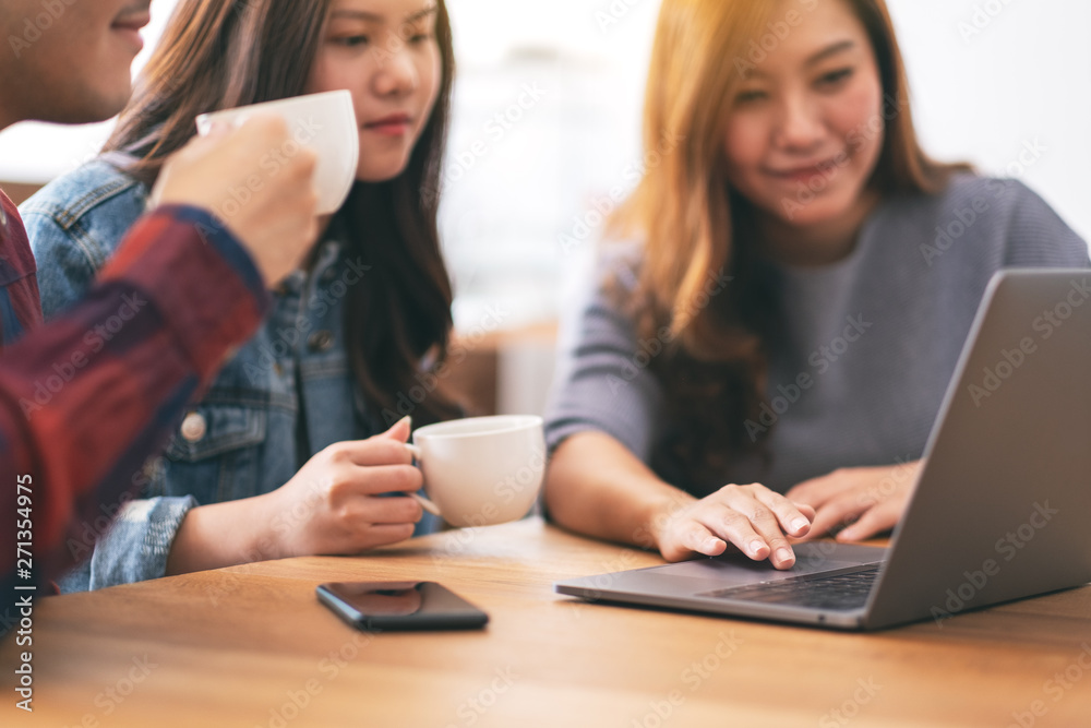 Three young asian people drinking coffee while using and looking at the same laptop computer