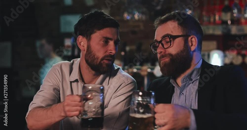 Two old friends drinking draft beer and talking in the sport bar. Friends sitting at bar counter, drinking beer and talking in beer pub.
