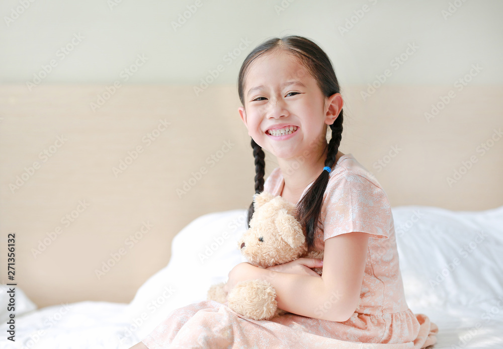Smiling Asian little girl cuddle teddy bear sitting on the bed at home. Smiling Asian little girl cuddle teddy bear sitting on the bed at home.