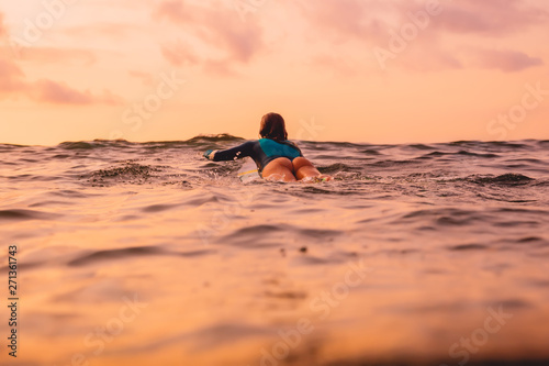 Beautiful surfgirl on a surfboard floating in ocean. Surfing at sunset