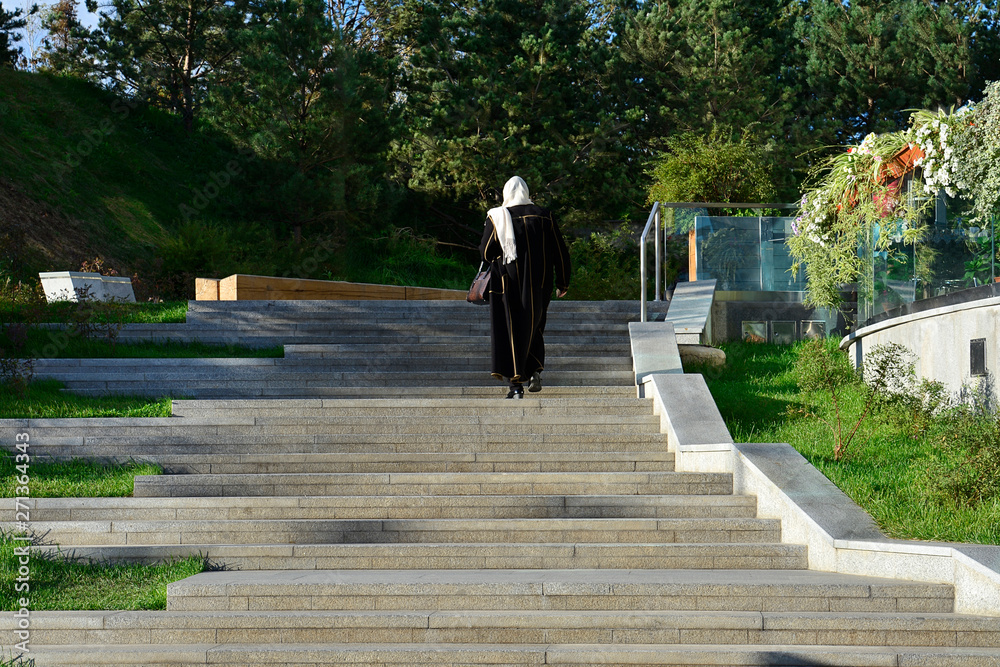 A Muslim woman climbs up the stairs to the terrace of a street cafe. A Muslim woman climbs up the stairs to the terrace of a street cafe.