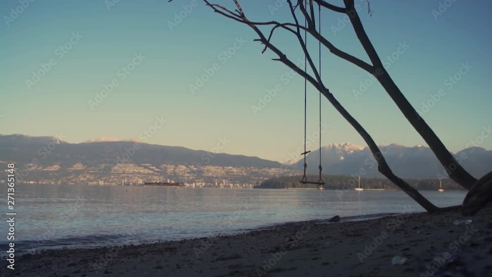 A SLOW MOTION FORWARD MOVING DOLLY SHOT of a Lonely Swing Hanging from a Tree, West Vancouver is Seen in the Distance A SLOW MOTION FORWARD MOVING DOLLY SHOT of a Lonely Swing Hanging from a Tree, West Vancouver is Seen in the Distance