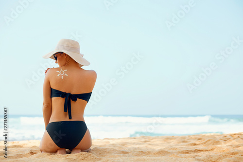 Beautiful Woman in Bikini Applying Sun Cream on Tanned  Shoulder. Sun Protection. Skin and Body Care. Girl Using Sunscreen to Skin. Portrait Of Female Holding Suntan Lotion and Moisturizing Sunblock