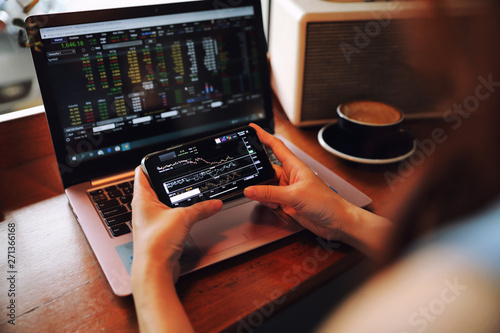 Female hand with smartphone trading stock online in coffee shop , Business concept