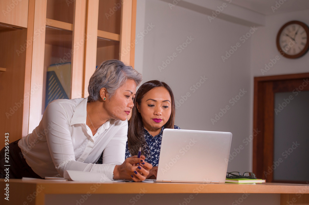 two women work colleagues or business partners working together reading on laptop computer in job cooperation and collaboration two women work colleagues or business partners working together reading on laptop computer in job cooperation and collaboration