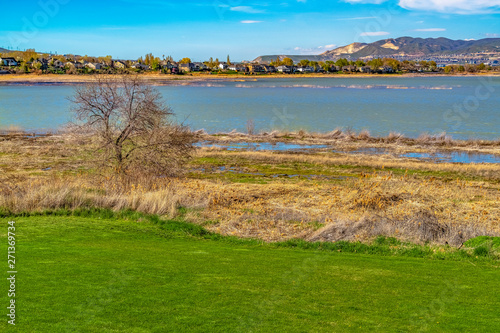 Bright green grassy field in front of a lake that reflects the blue sky overhead © Jason