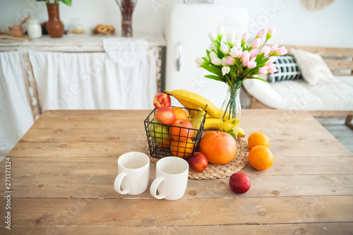Concept breakfast made from fruits and coffee or tea. Oranges, bananas, cups, peaches on a textural large wooden table against a background of rustic or Scandinavian cuisine
