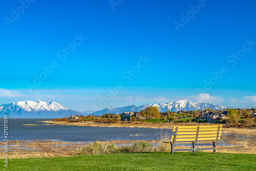 Bench on a grassy field overlooking lake and snowy mountain against blue sky