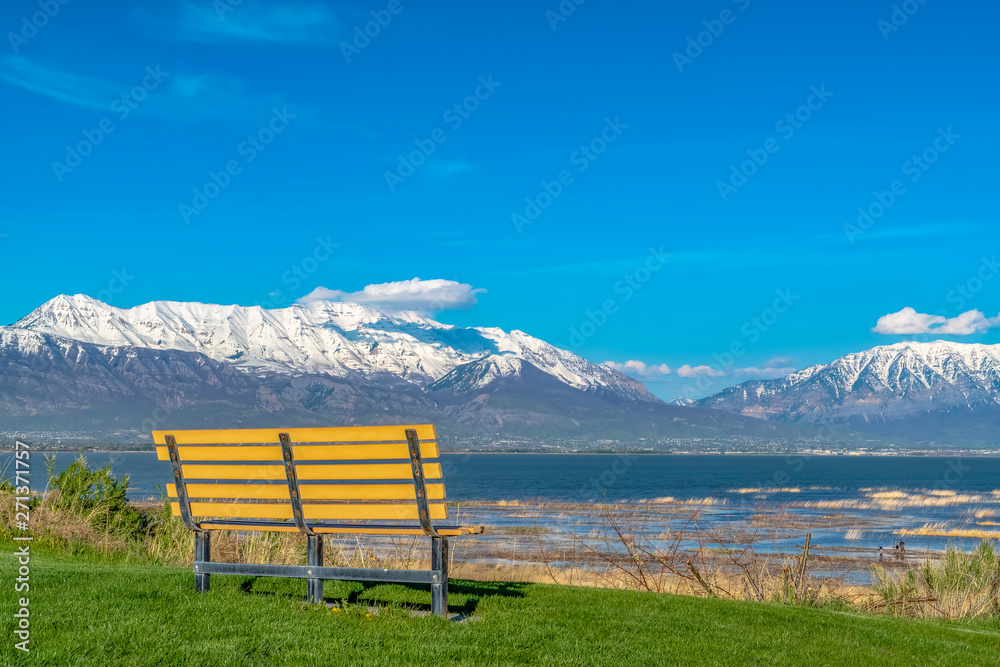 Empty bench with view of snow capped mountain towering over lake and valley