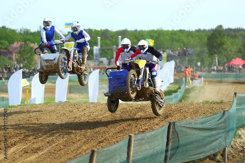 Sidecar motocross athletes overtaking in the air jump on the dirt track  photo